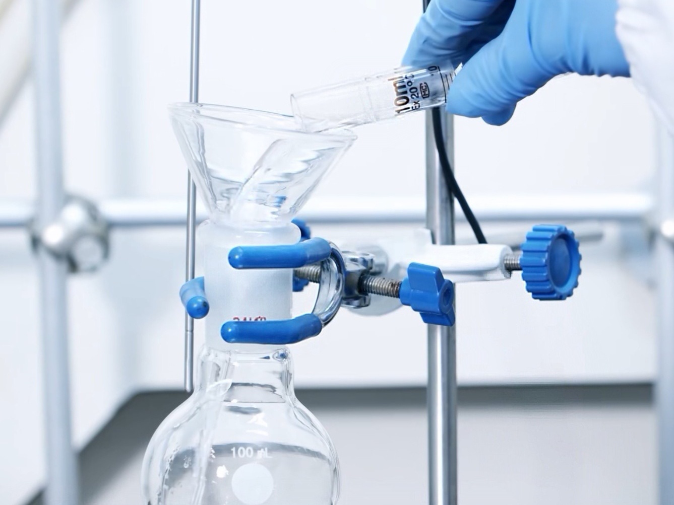Macro photograph focusing on a glass laboratory joint secured by a blue joint clip, with a clear liquid pooling inside.
